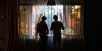 Two shadowed people look out of window , while adjusting curtains