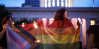 Two transgender rights advocates hold a large progress pride flag in front of the Ohio Statehouse