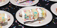Rectangular slices of confetti-style birthday cake cut up on white disposable plates with silver forks.