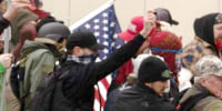 Aaron Sauer, in black baseball cap and a blue and white face covering, holds pepper spray during the Capitol riots on Jan. 6, 2021.