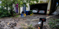 A resident tries to sweep mud and debris from the driveway of his home