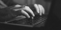 A blackand white photo of a man's hands on a laptop 