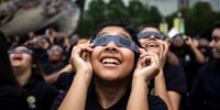 Students smile as they watch the eclipse with their glasses on.