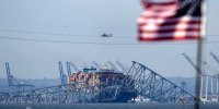 An American flag flies on a moored boat as the container ship Dali rests against wreckage of the Francis Scott Key Bridge, in Baltimore