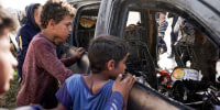 People gather around the carcass of a car used by aid group World Central Kitchen.