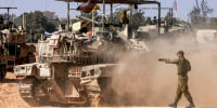 An Israeli army soldier gestures behind a moving main battle tank 