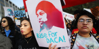 Supporter holding "rise for DACA" sign in group. 