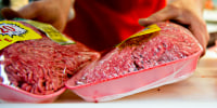 An employee stocks packages of ground beef at a supermarket.