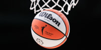 A detail of the WNBA logo is seen on a basketball falling through a hoop