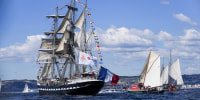 Belem, a three-masted sailing ship, adorned with flags from various countries, sails in the sea