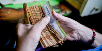 Hands flip through a thick stack of pesos