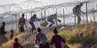 Migrants cross through a barbed-wire fence.