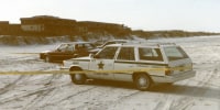 Police vehicles parked on the beach behind police tape