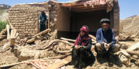 An Afghan couple sit near to their damaged home