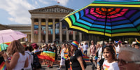 Attendees with umbrellas and rainbow flags march during Pride event. 