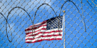 A U.S. flag flies behind barbed wire.