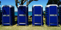 A row of outdoor four blue toilet cubicles at an event.