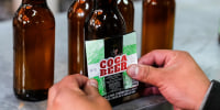 A worker puts a label reading "Coca Beer" on coca leaf-flavored beer bottles
