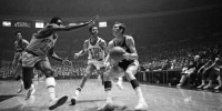 Jerry West of the Los Angeles Lakers crashes against Willis Reed of the New York Knicks as he passes off to Wilt Chamberlain in the opening minutes of the first game of the NBA Championship playoff series in Inglewood, Cal., on May 1, 1973.
