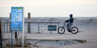 A man rides his bicycle down the boardwalk at a deserted Jacob A. Riis Park.