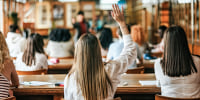 Female student raising hand to ask a question in a classroom