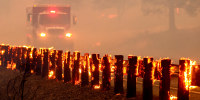 A fire engine drives past flaming highway guard rails.