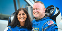 Suni William and Butch Wilmore stand and smile for a photo together in their Boeing space suits