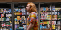 A shopper walks in front of beer in a refrigerator