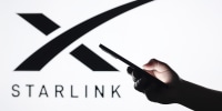 In this photo illustration, the Starlink logo seen in the background with a silhouette hand holding a smartphone.