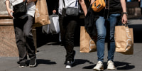 Shoppers carry Macy's bags while walking on the sidewalk