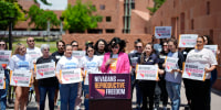 Lindsey Harmon speaks outside behind a podium while people stand on either side of her holding signs that say "Nevadans for Reproductive Freedom"