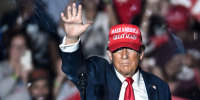 Donald Trump waves on stage behind protective glass