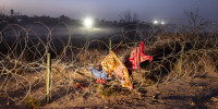 Discarded blankets and clothing hang caught in razor wire outside at night