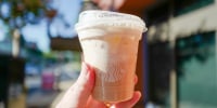 A person holds a cup of Starbucks Iced Apple Crisp Nondairy Cream Chai 