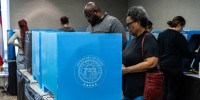 Voters cast their ballots inside of a room at tables with blue dividers