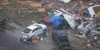 An aerial view of damaged cars surrounded by debris on the road and a lawn