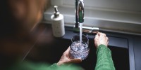 Close up of a senior woman's hand filling a glass of filtered water right from the tap in the kitchen sink at home