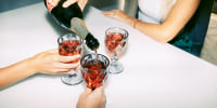 A woman pours red sparkling wine into friends' glasses.