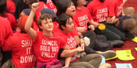 Protestors sit on the ground and link arms wearing shirts that say "Council Sold Out Philly"