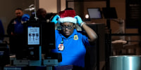 A TSA agent adjusts their holiday hat between checking traveler's documents through in line for security at Love Field airport in Dallas, Texas on Dec. 20, 2024. 