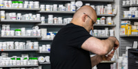 A pharmacist works next to a wall of medications