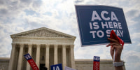 A sign is held up that reads "ACA Is Here To Stay" front of the U.S. Supreme Court.