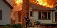 A person turns uses a garden hose in an effort to save a neighboring home.