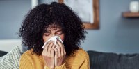 Shot of a young woman blowing her nose with a tissue at home