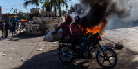 Men on a motorcycle drive past by burning tires 