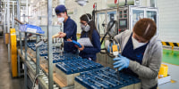 Workers wearing masks weld acid batteries in a factory