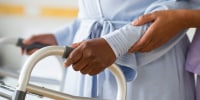 Nurse helping woman use walker in hospital hallway