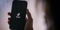 A person holds a phone with the TikTok logo.