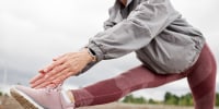 Fit Mature Woman Stretching Muscles Folding Torso over Leg in Park