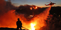 A helicopter drops water as the Palisades Fire grows